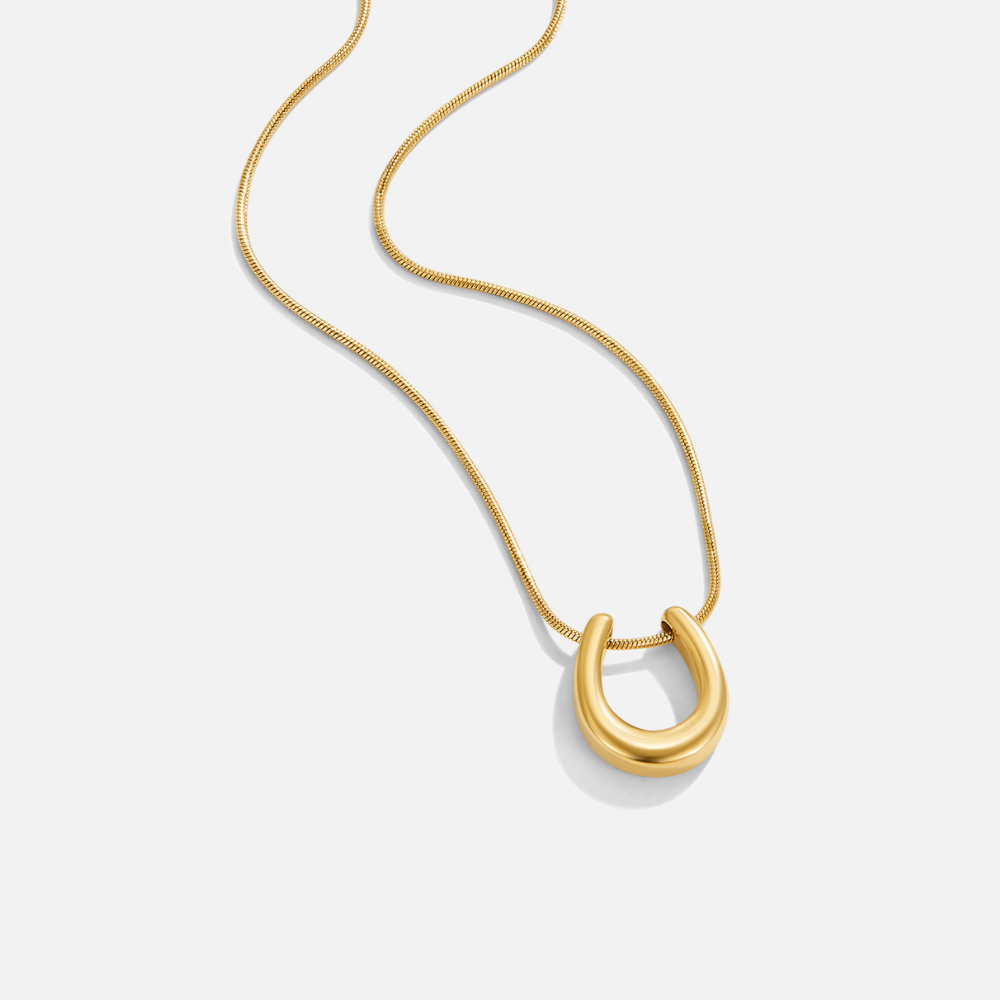 Golden Horseshoe Necklace, laid flat on white, thick gold U-shaped pendant on fine chain