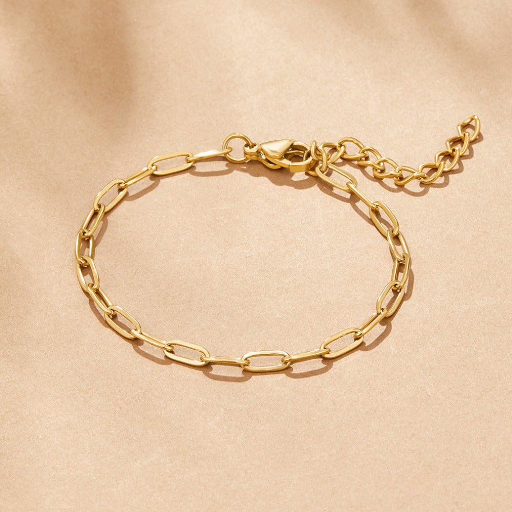 18K Gold Paperclip Charm Bracelet, laid flat on beige fabric, gold chain with lobster clasp