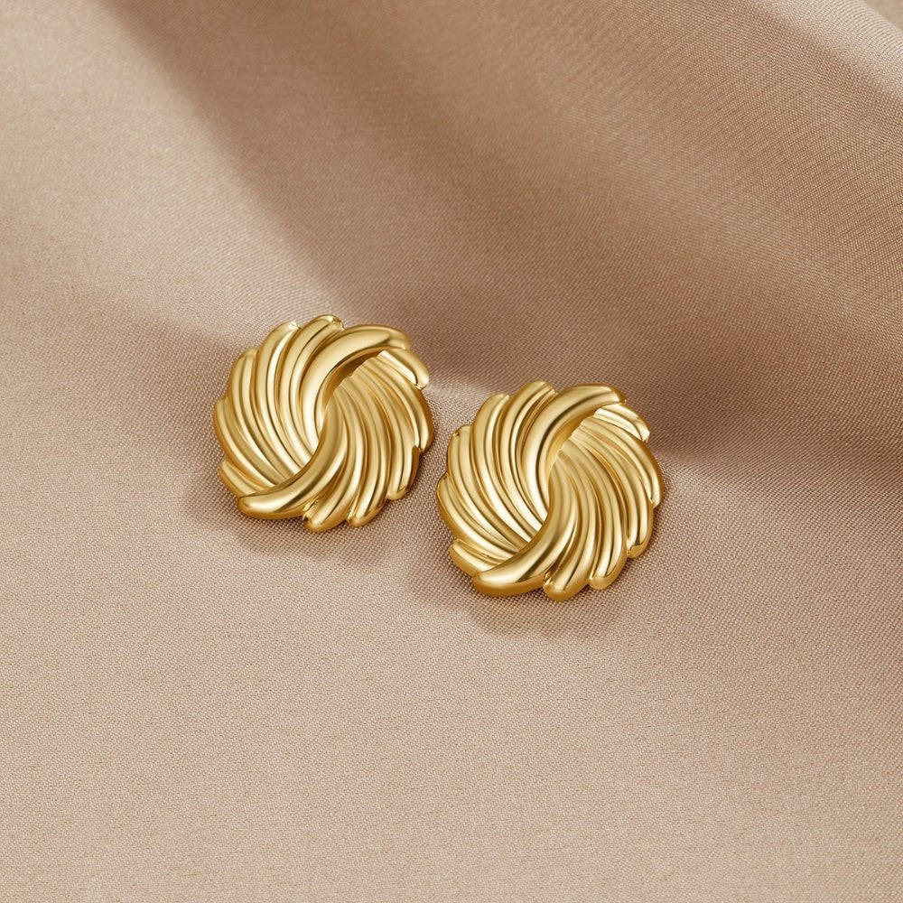 18K Gold Spiral Earrings, a pair of swirled gold stud earrings lying on beige satin