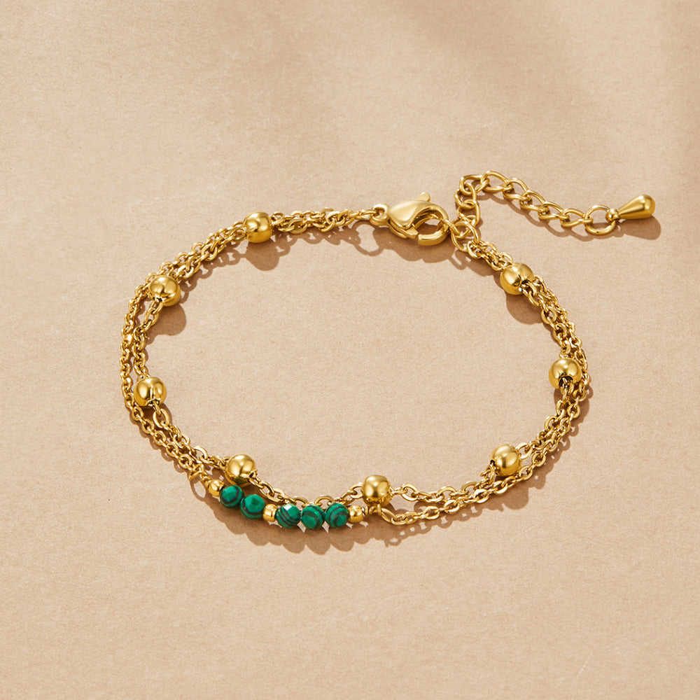 Alfa Green Malachite Bead Bracelet, laid flat on a beige surface, two gold chains with green beads