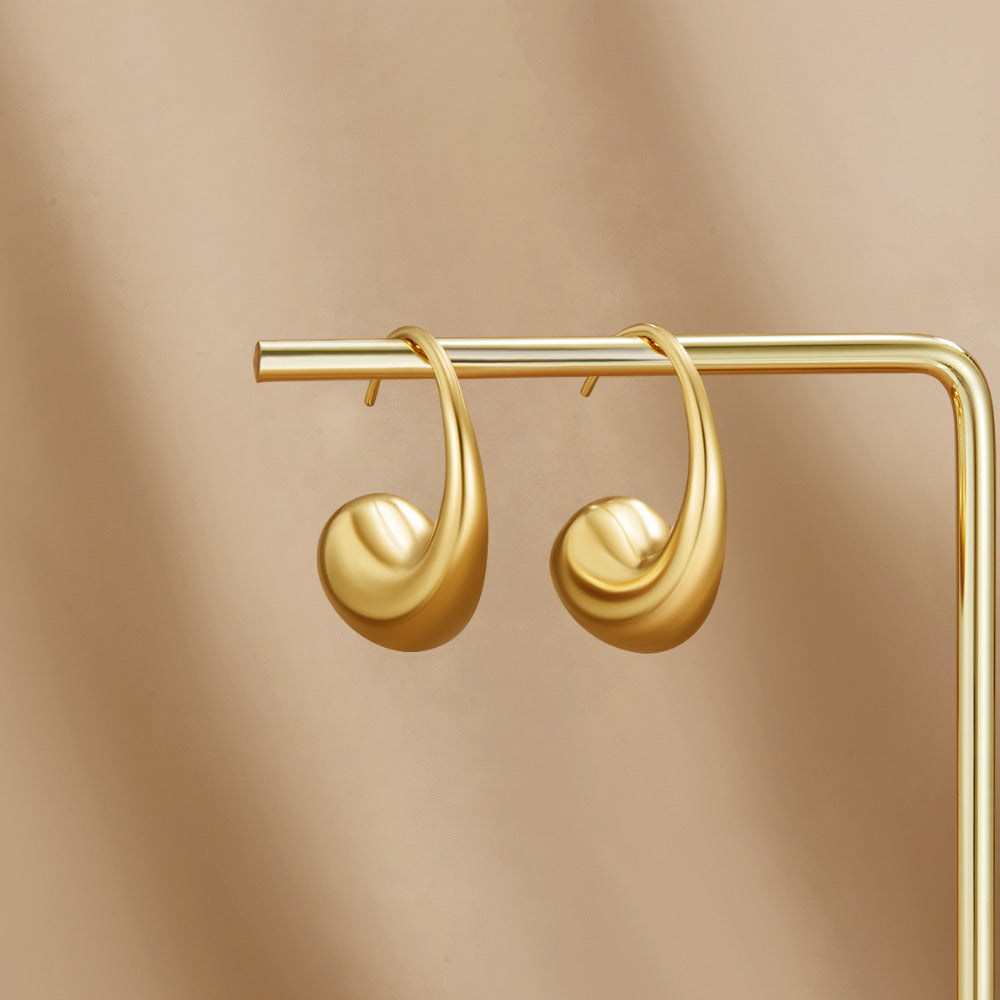 Chunky Gold Teardrop Earrings, a pair of earrings hanging on a gold display stand against beige fabric