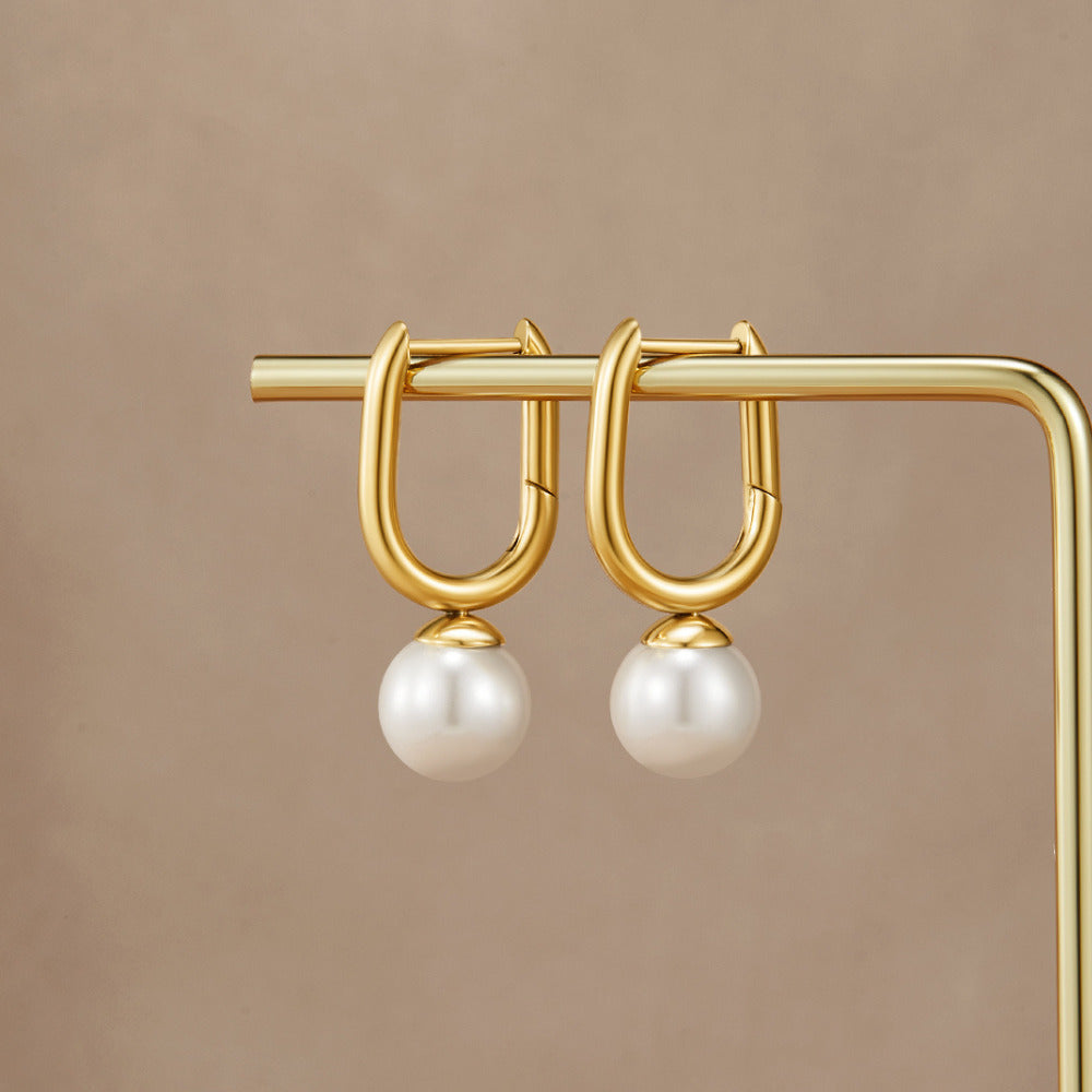 Cora Pearl Hoop Earrings, a pair of gold U-shaped hoops with pearl drops, displayed on a gold stand