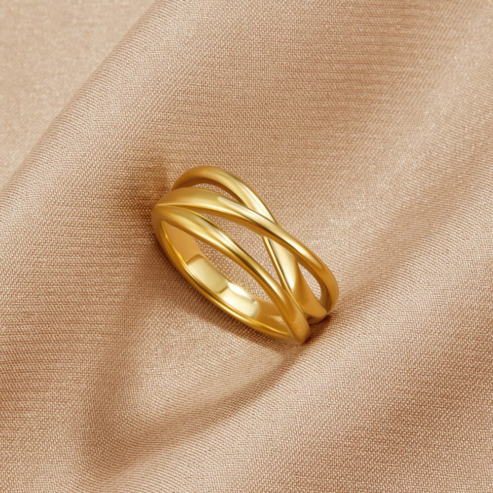 Entwined Maisie Gold Ring, lying on a draped beige satin cloth, crossed gold bands