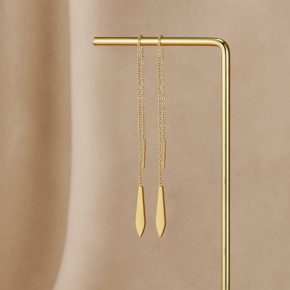 Gold Dakota Tassel Earrings, threader earrings hanging from a gold display stand on beige fabric