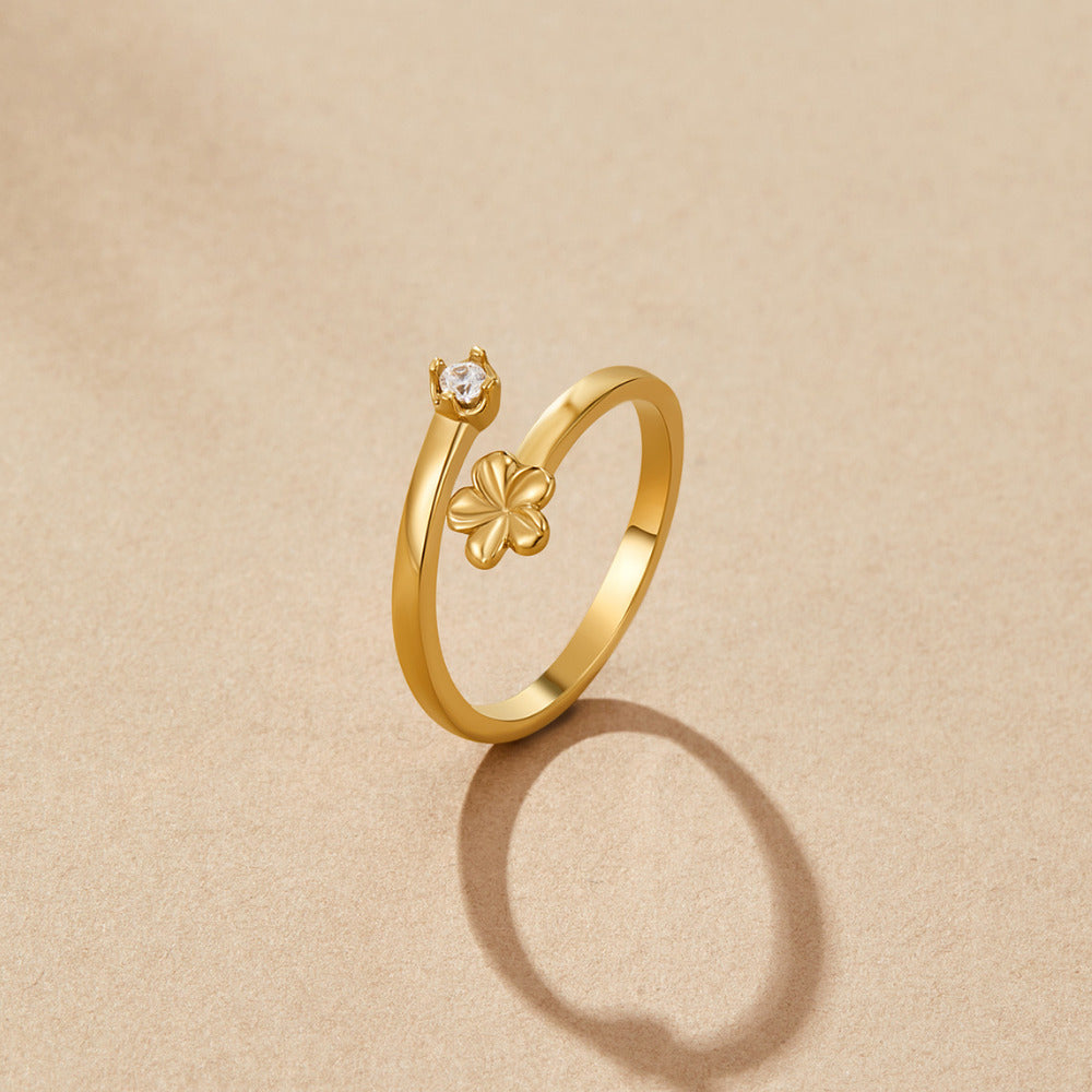 Golden Bloom Petal Ring, open gold ring on beige surface with clover charm and clear stone