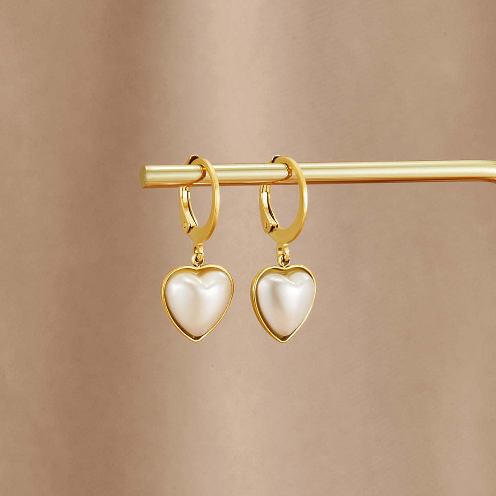 'Pure Heart' Pearl Hoop Earrings, a pair of hanging on a gold rod against a beige backdrop