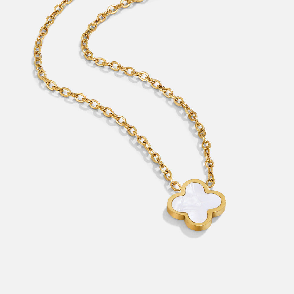 White Clover Necklace, gold chain necklace laid on a white surface, close-up on the clover pendant