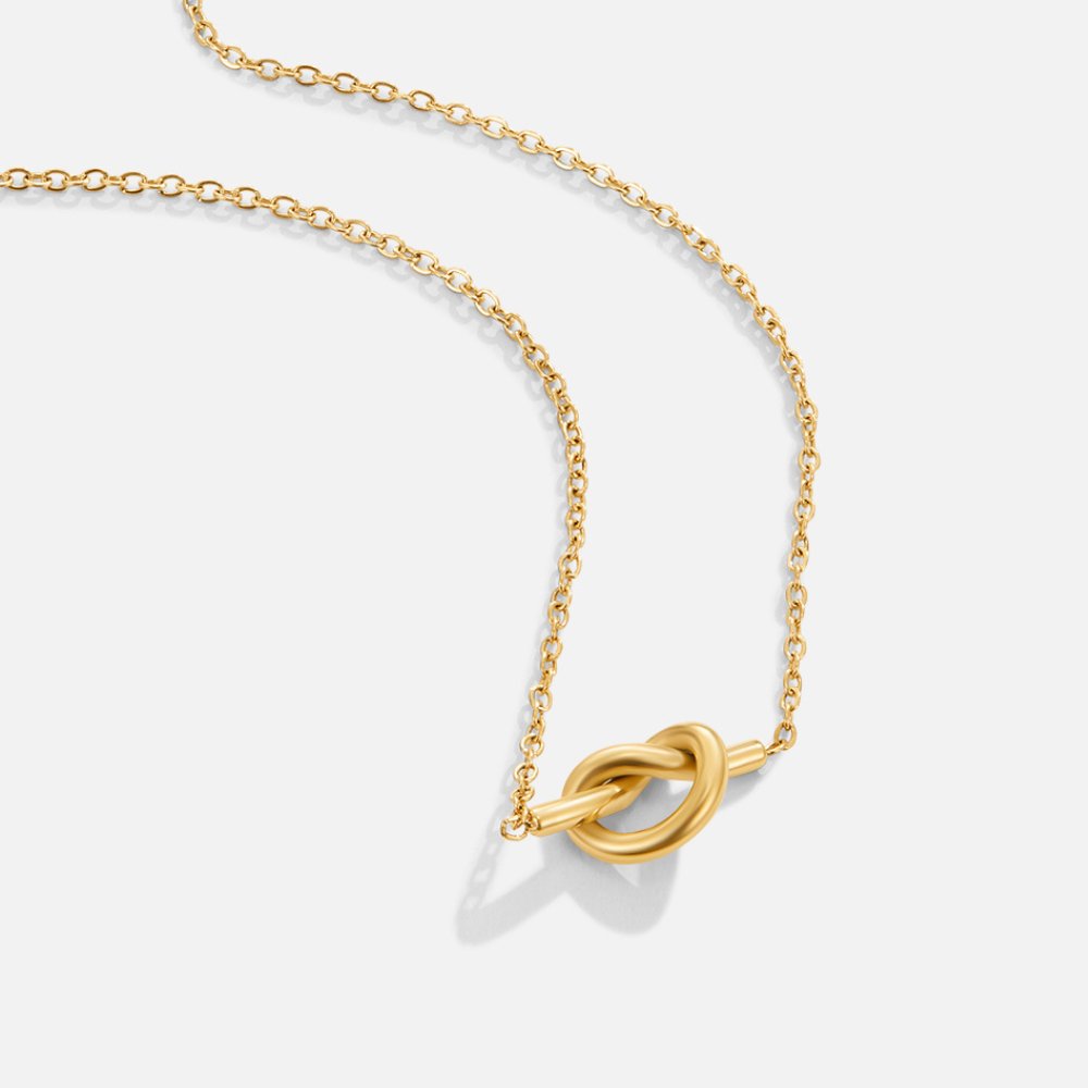 Adela Knot Necklace, gold chain necklace laid flat on a pale background, with a knot pendant