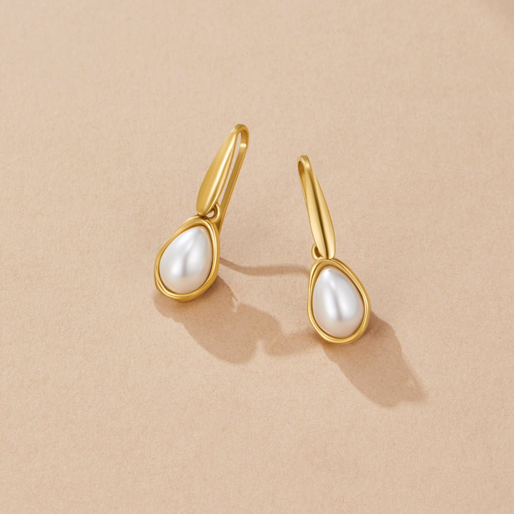 Agatha Pearl Drop Earrings, pair of gold drop earrings with teardrop pearls on beige surface