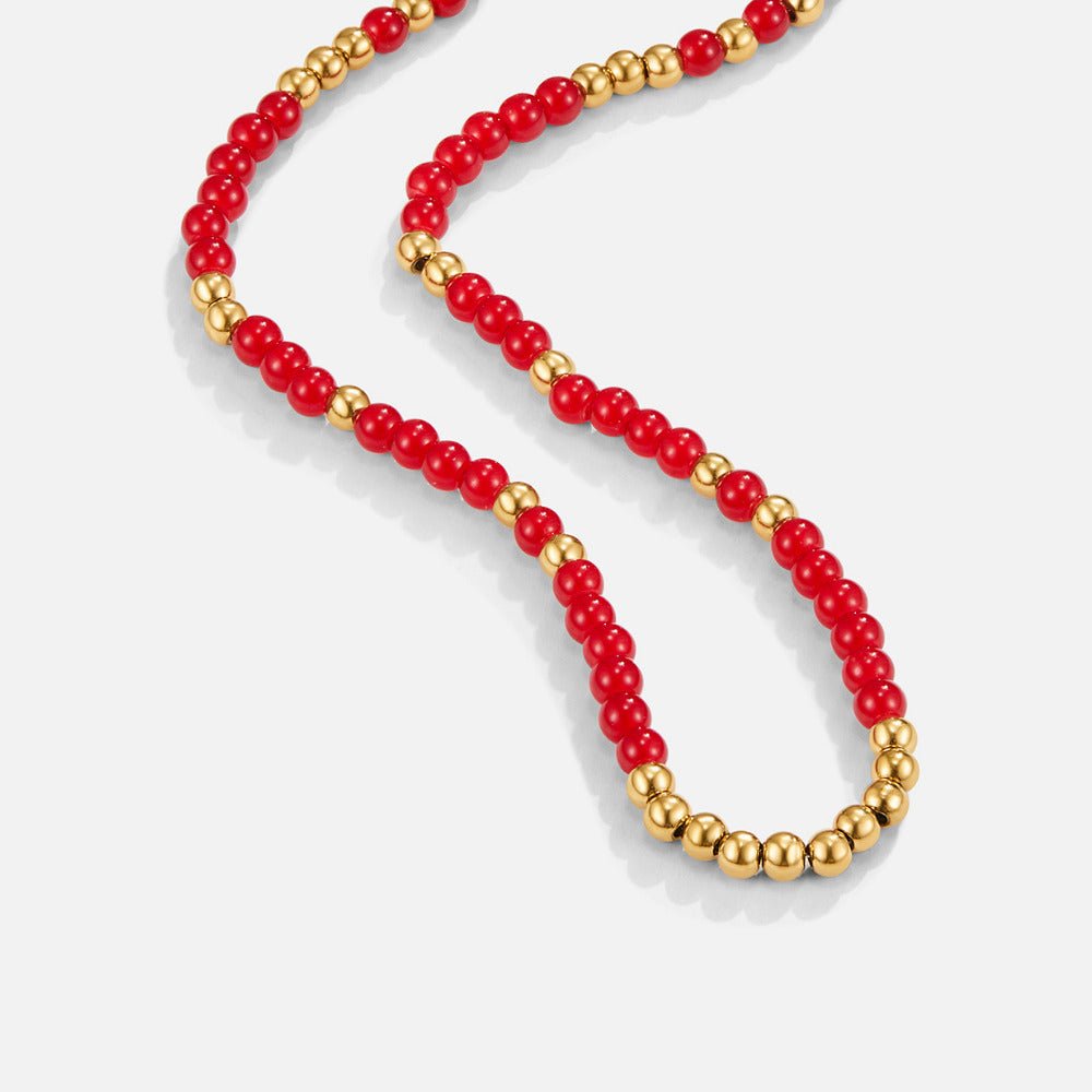 Alea Red Coral Bead Necklace, laid out on a light grey surface, red beads with gold spacers