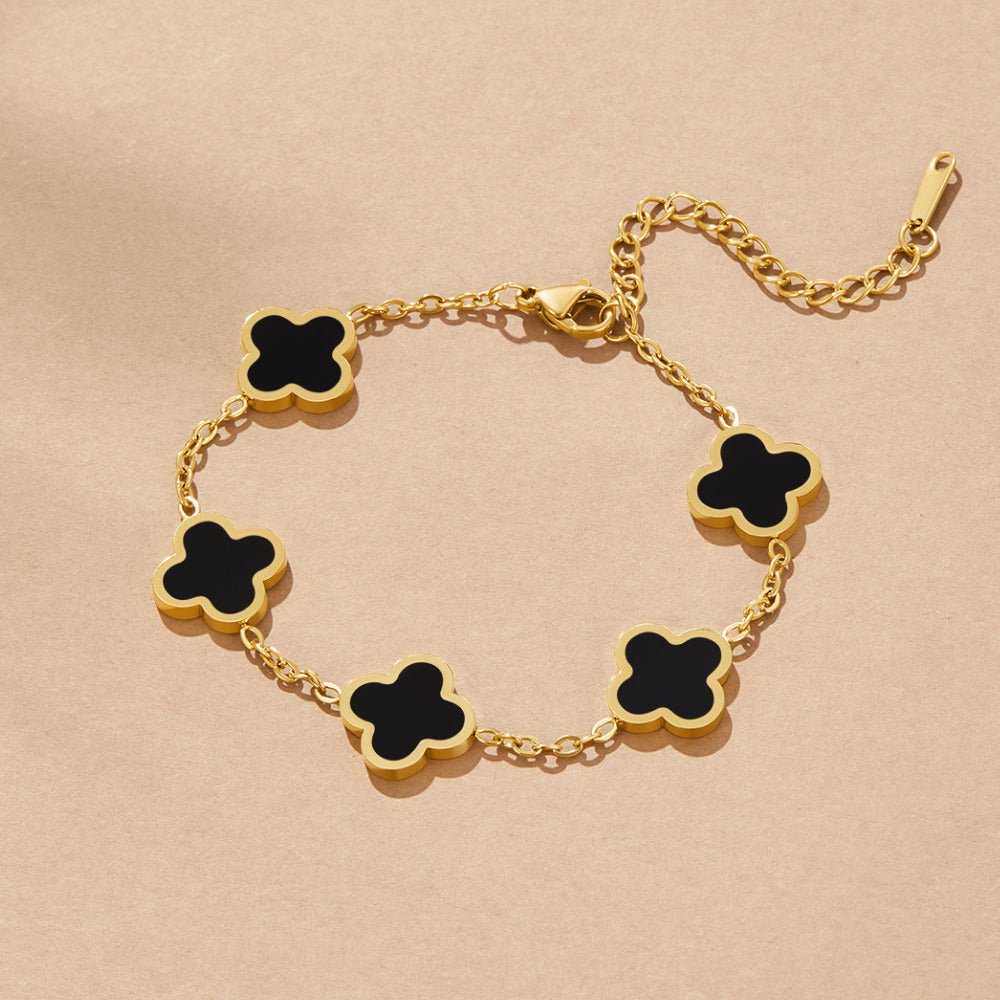 Black Clover Bracelet, flat lay on beige, five black clover motifs with gold edges on a gold chain