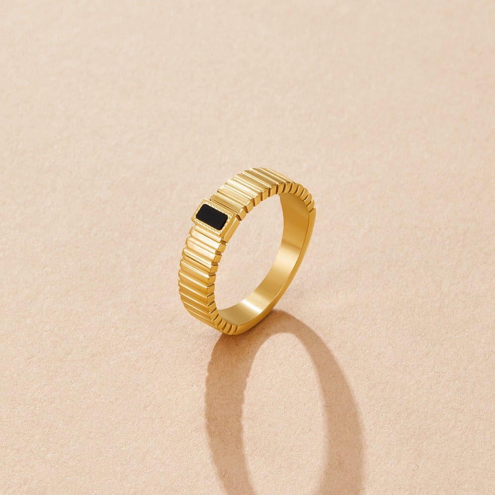 Black Crystal Ribbed Ring, standing upright on beige surface, gold ribbed band with black stone