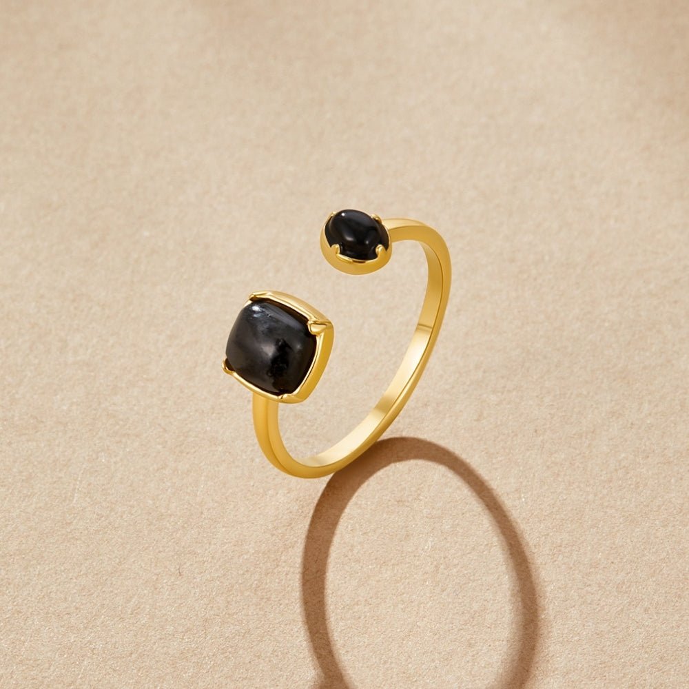 Black Orion Wrap Ring, open gold ring with two black cabochon stones on sand background