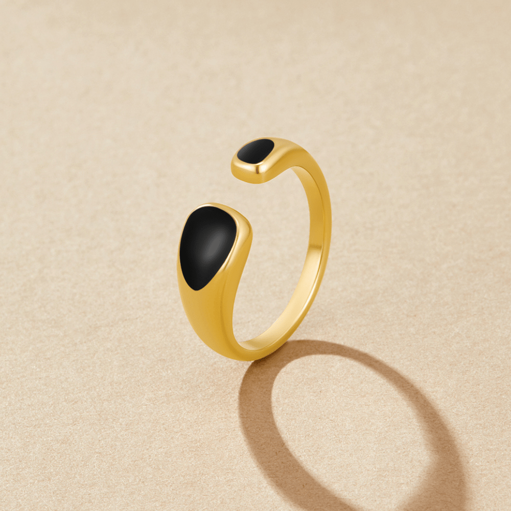 Black Sahara Wrap Ring, open gold ring with two black enamel ends on beige surface