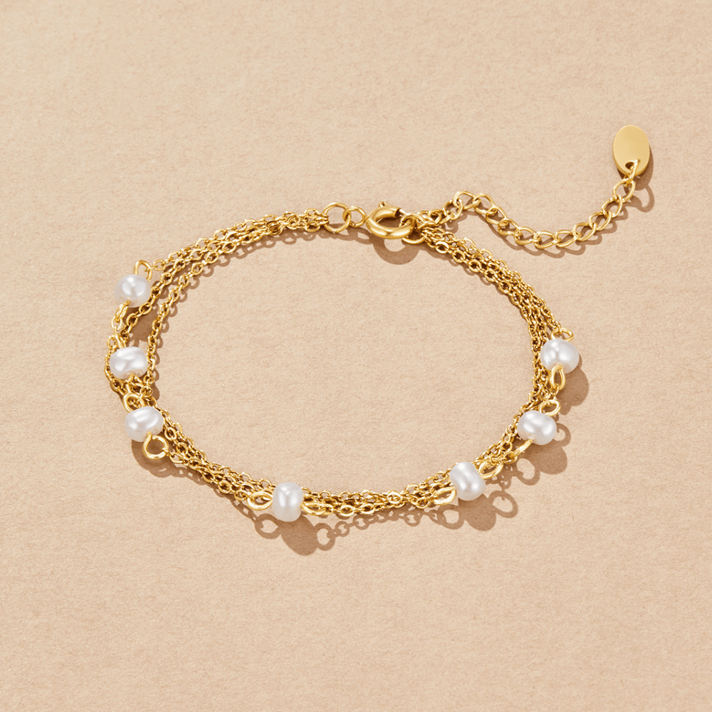 Callie Layered Pearl Bracelet, flat lay of gold chain bracelet with white pearls on beige