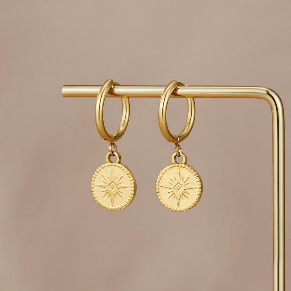 Celestial Gold Coin Earrings, hung on a gold display bar against a taupe backdrop