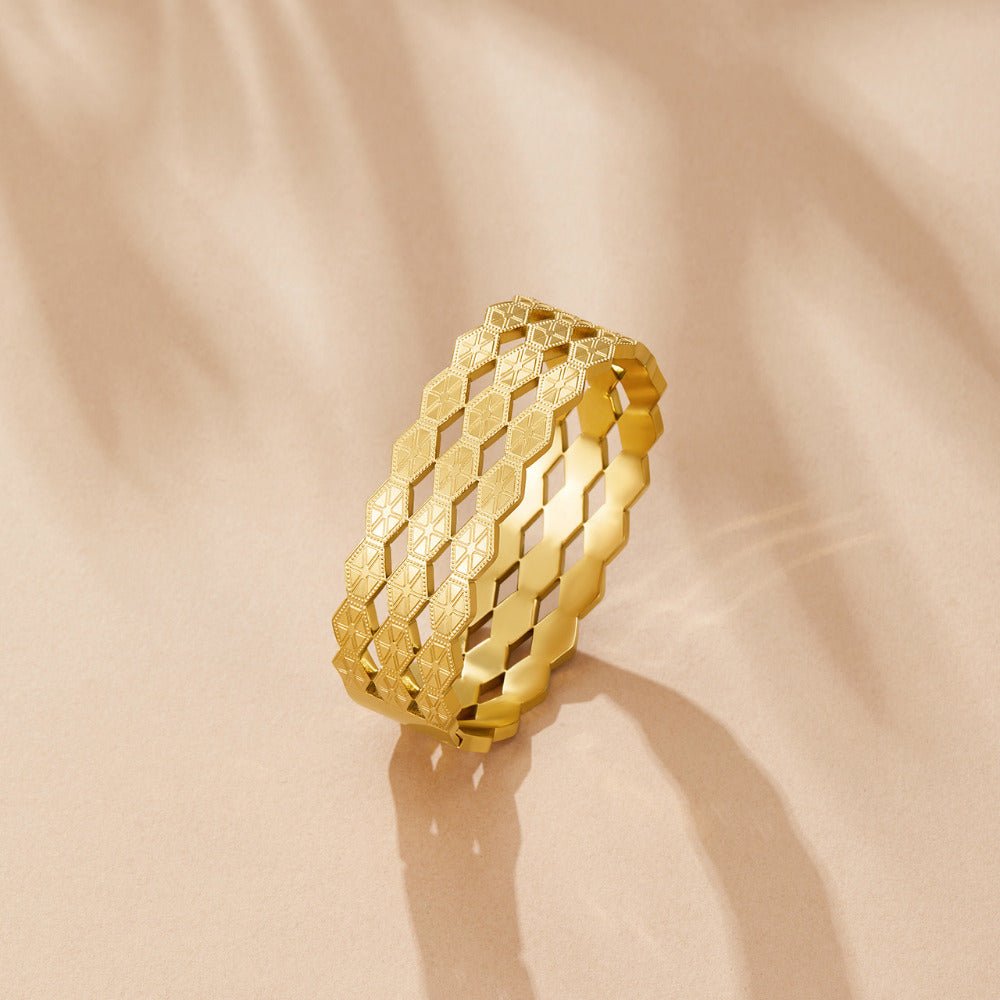 Celine Geometric Gold Bangle, standing upright on a peach surface, casting a shadow; gold hexagon-patterned band