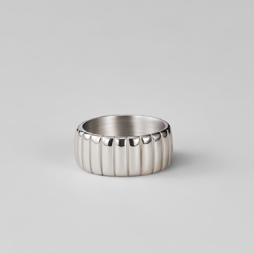 Chunky Calira Silver Ring, wide silver band with vertical ridges, standing upright on grey backdrop