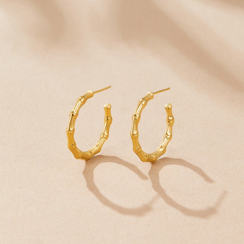 Classic Hoop Bamboo Earrings, a pair of gold hoops lying on a beige surface, casting shadows