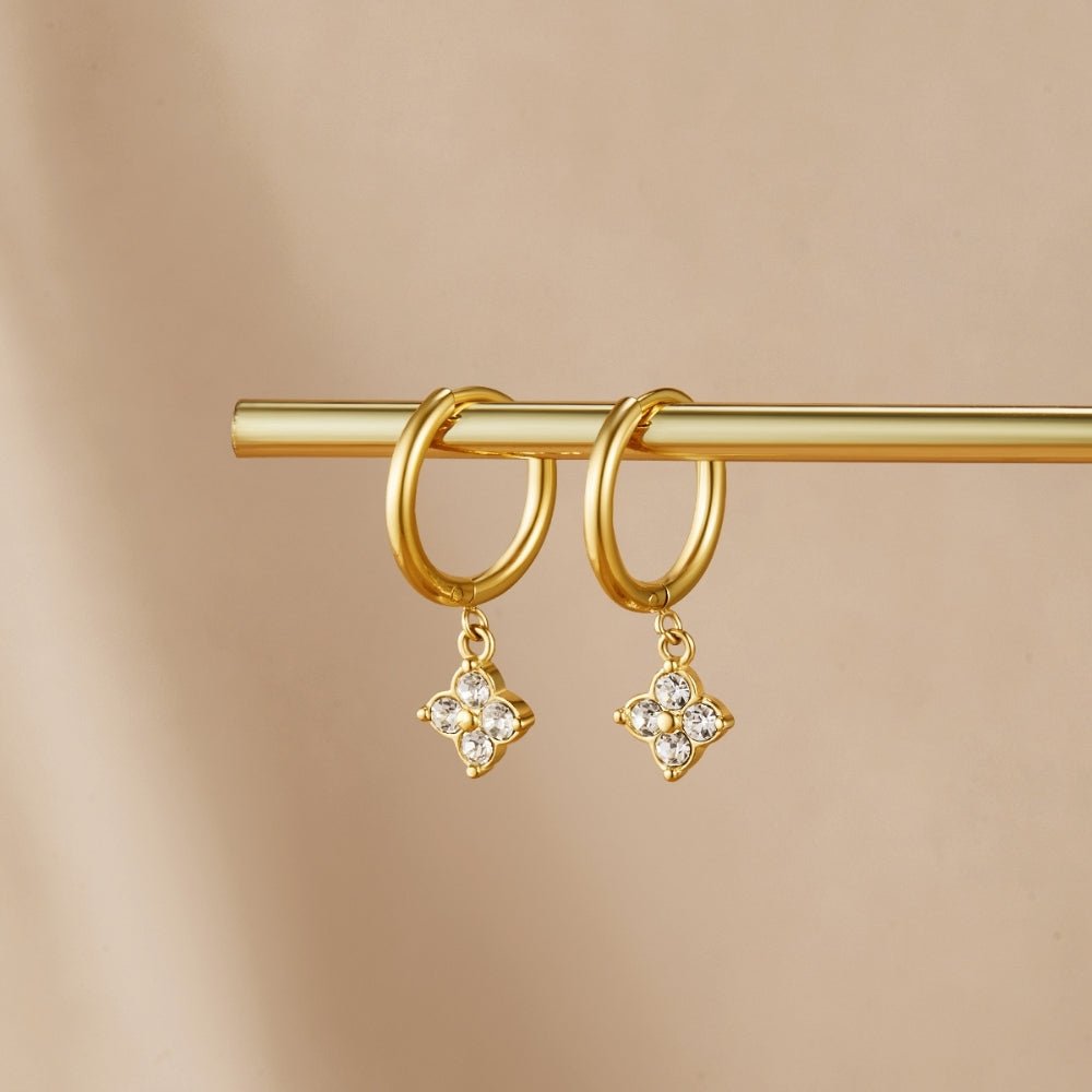 Crystal Four Leaf Clover Drop Earrings, hanging from a gold bar on a beige backdrop, close-up pair