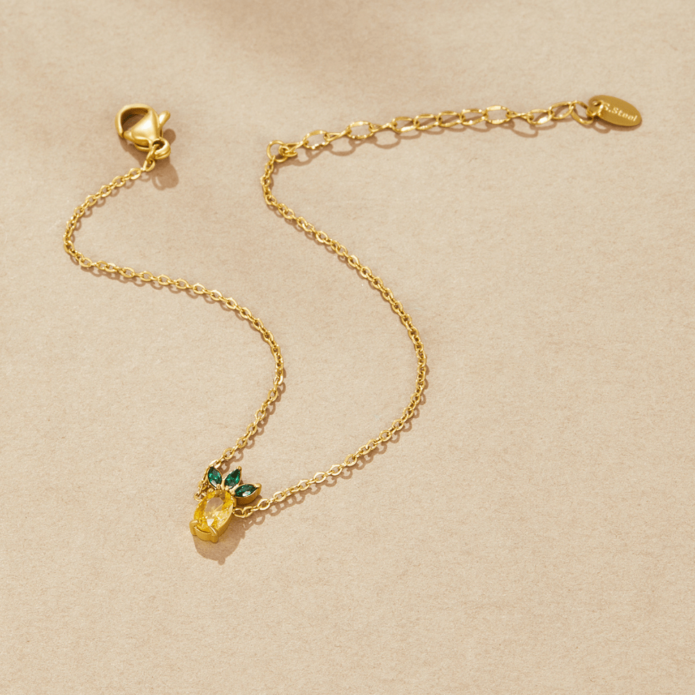 Crystal Pineapple Bracelet, laid flat on beige paper, gold chain with yellow and green stone charm