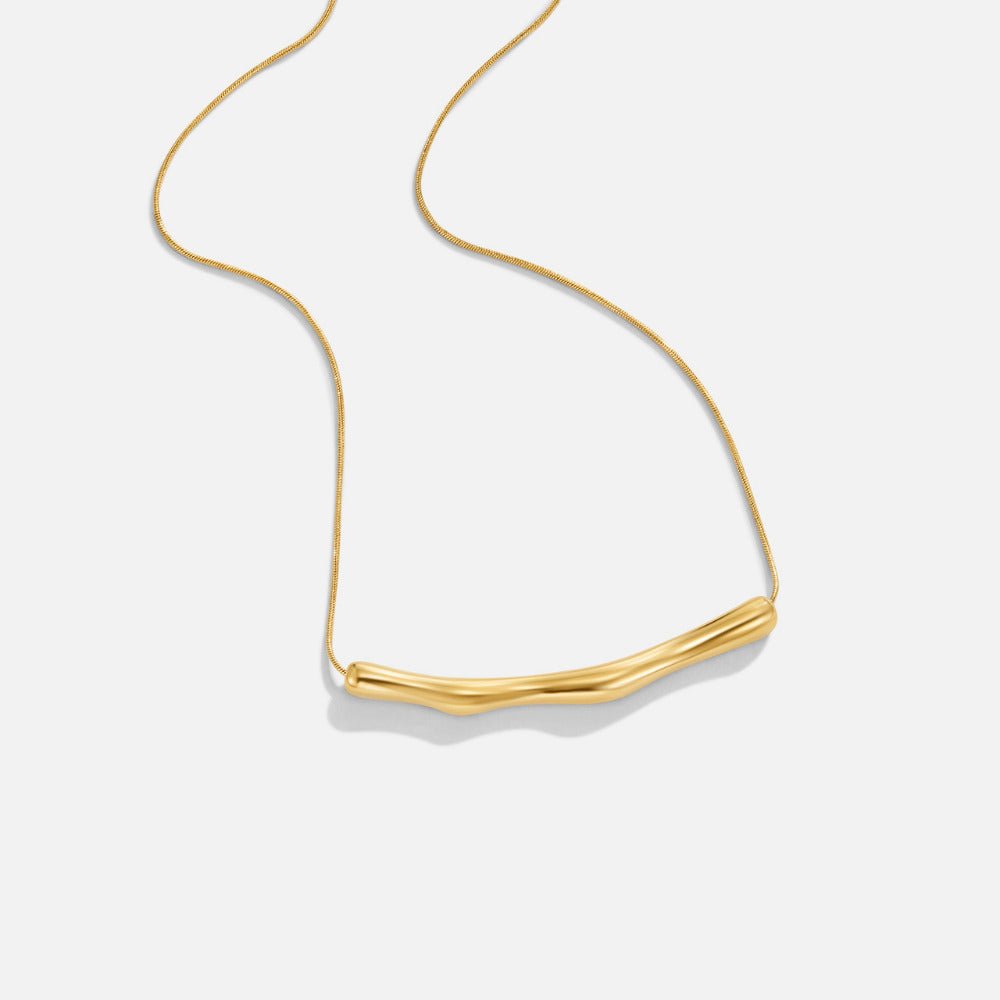 Deana Gold Bamboo Necklace, flat lay of a gold necklace with a curved bamboo-like bar pendant