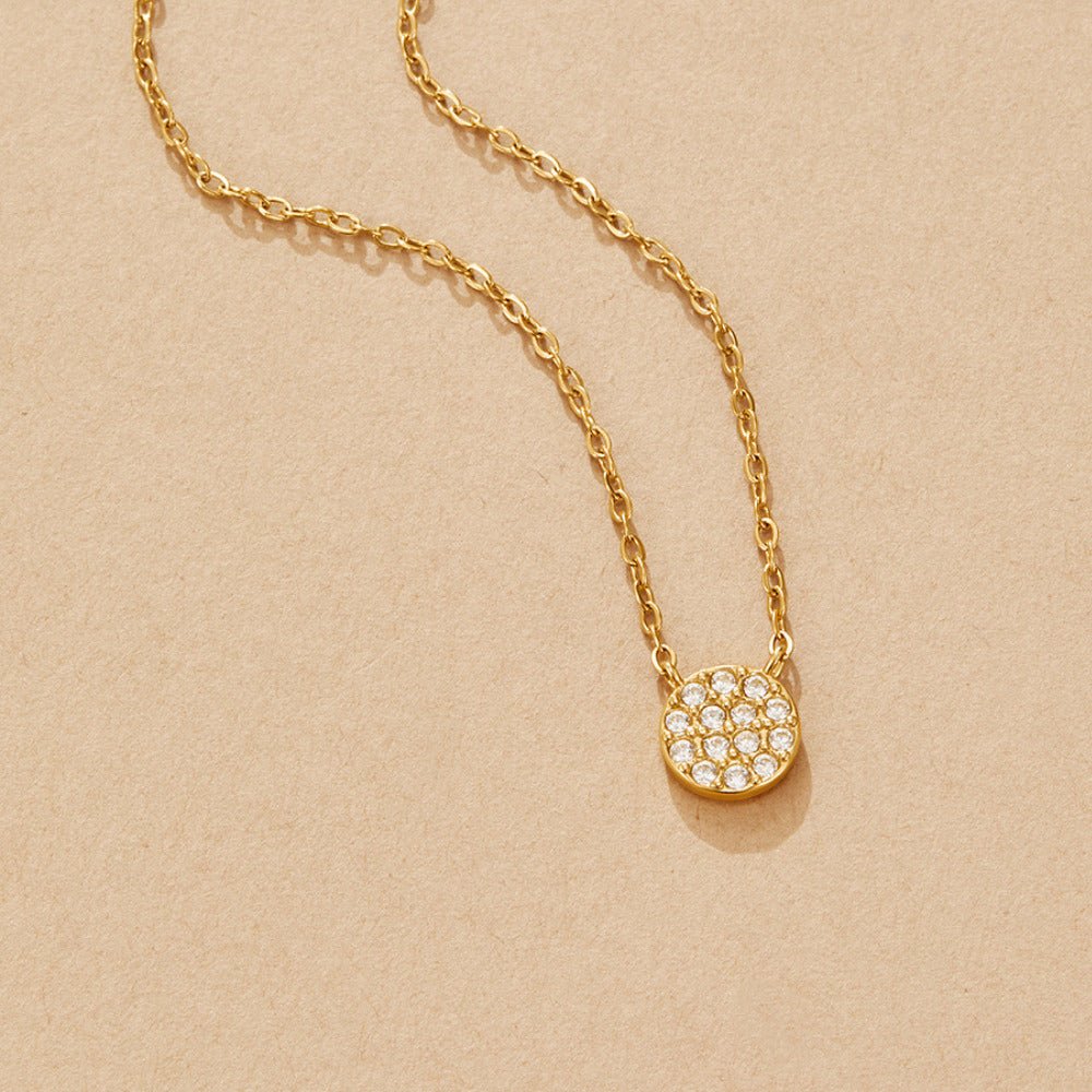 Elaine Crystal Disc Necklace, laid flat on a beige surface, gold chain with pavé disc pendant