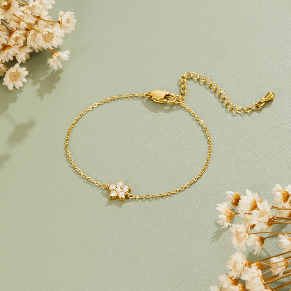 Elara Crystal Bloom Gold Bracelet, laid flat on sage green with dried white flowers, flower