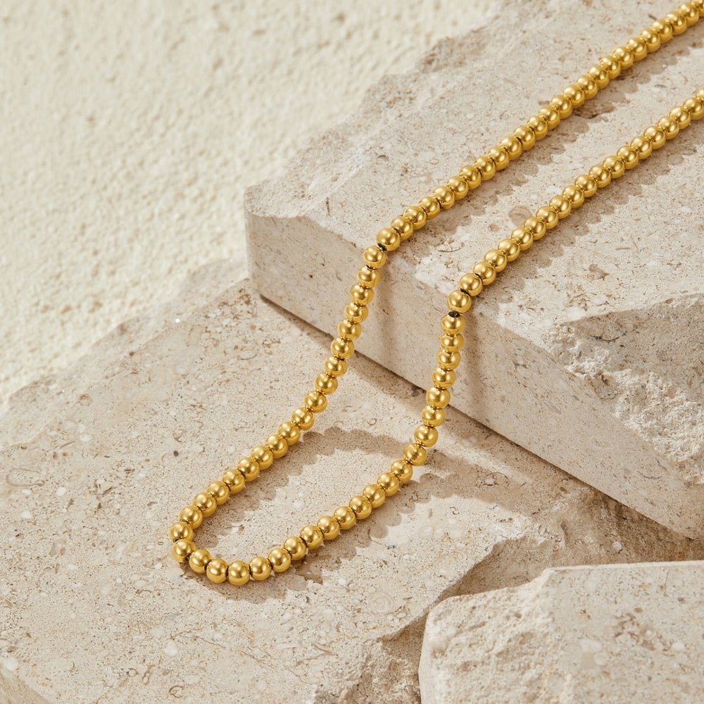Elena Gold Ball Chain Necklace, gold bead chain laid in a curve on pale stone blocks
