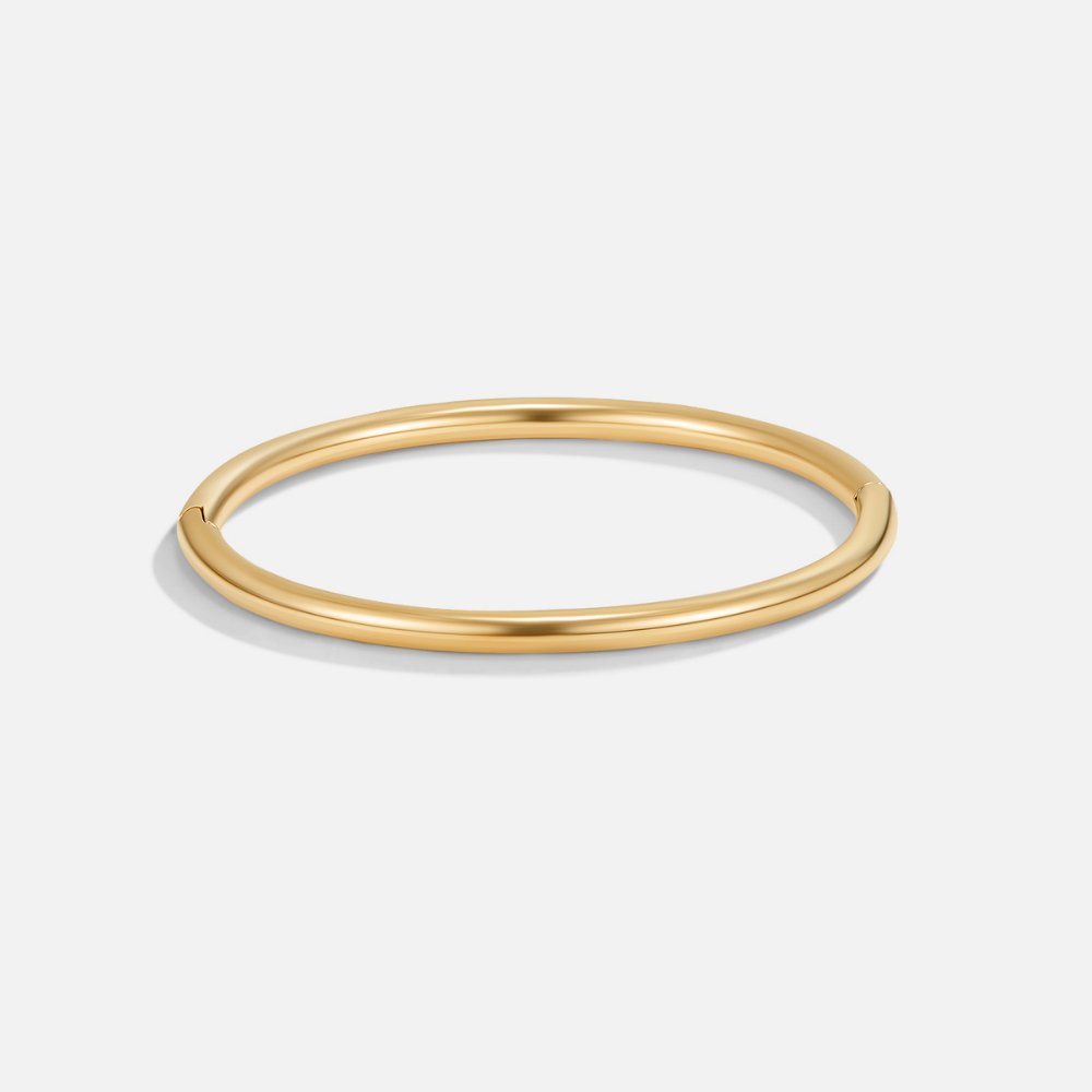 Eli Gold Bangle, polished gold bangle on a plain light grey background, seen from the side