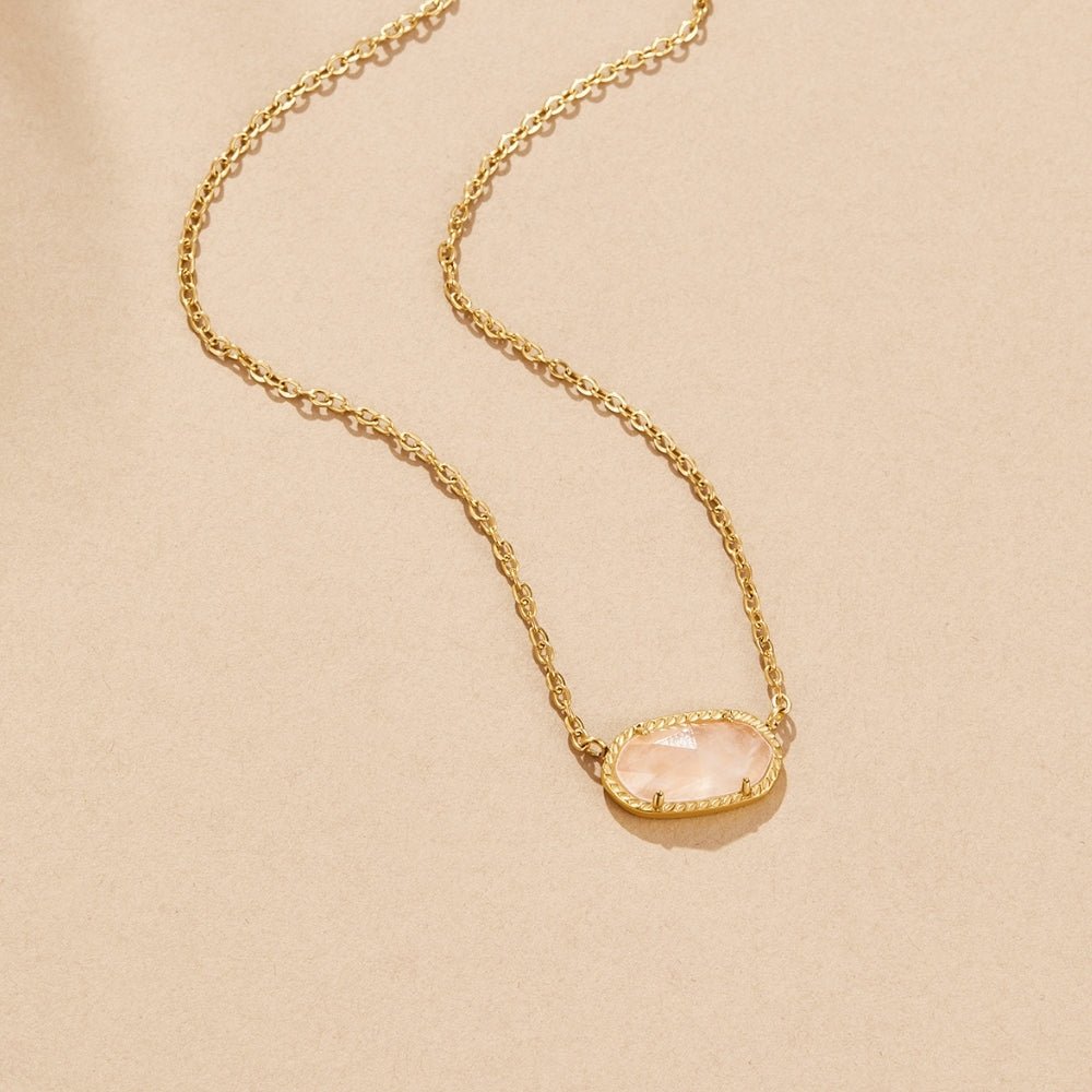 Ember Stone Pendant Necklace, laid flat on a beige surface, gold chain with pale pink oval stone