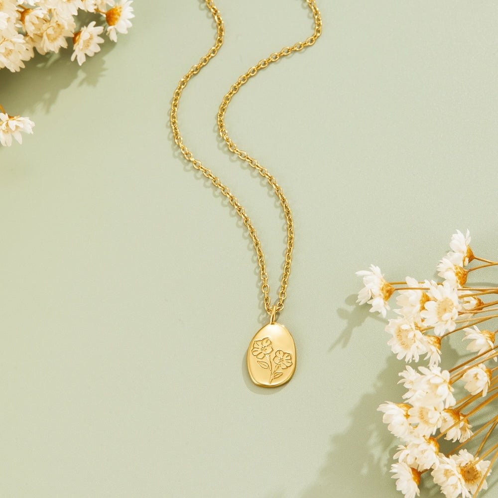 Engraved Wildflower Gold Necklace, laid flat on sage green with dried white flowers, oval