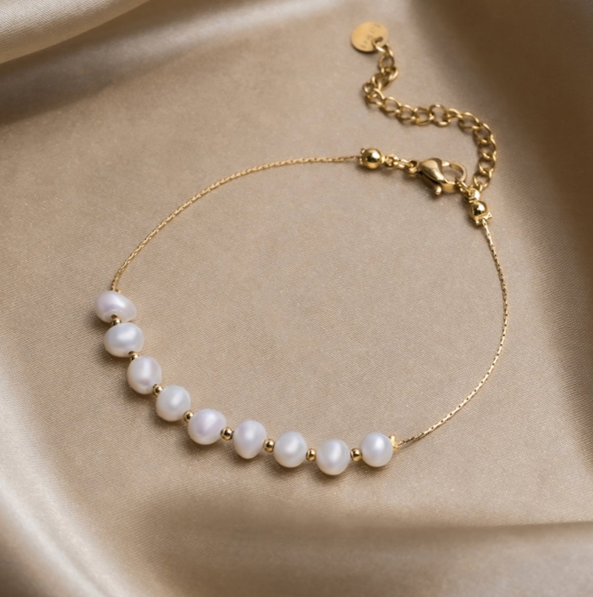 Eva Freshwater Pearl Bracelet, laid flat on cream satin with a row of white pearls and gold chain