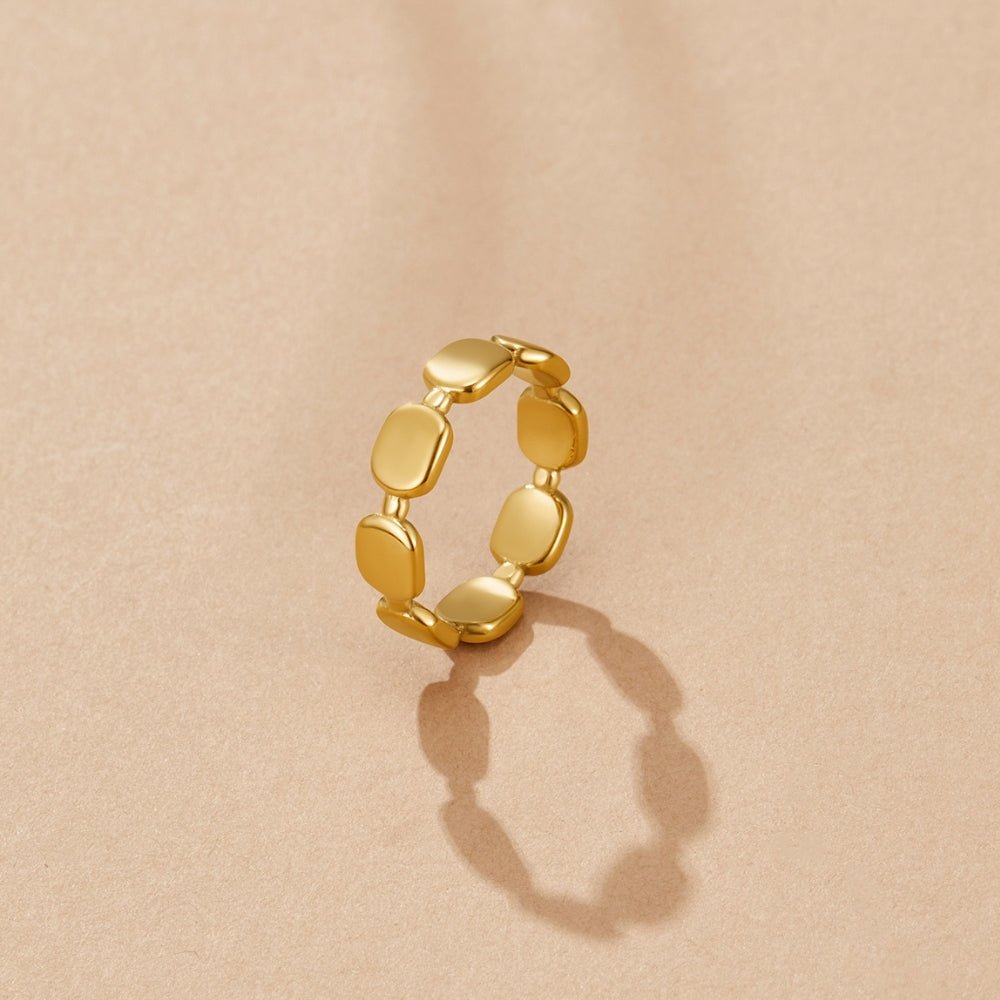 Florence Gold Band Ring, standing upright on a beige surface, with a shadow cast below