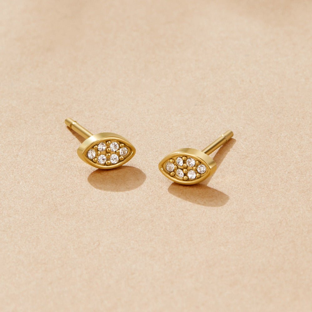 Gold Montana Stud Earrings, a pair of almond-shaped studs on a beige surface, pavΓ©-set with