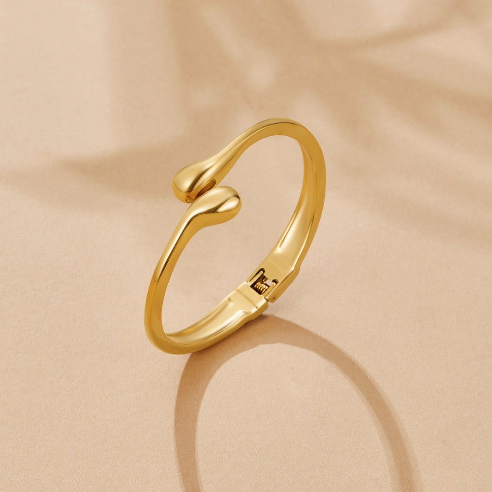 Gold Teardrop Bangle, polished gold bangle on beige surface, teardrop ends, hinged clasp visible