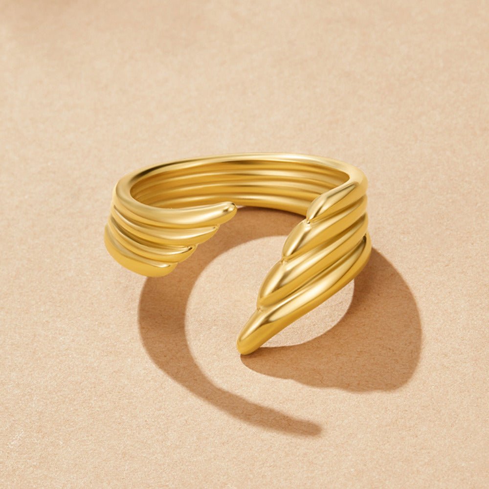Golden Angel Wing Wrap Ring, open wrap ring on a beige surface, ribbed gold bands, casting a shadow