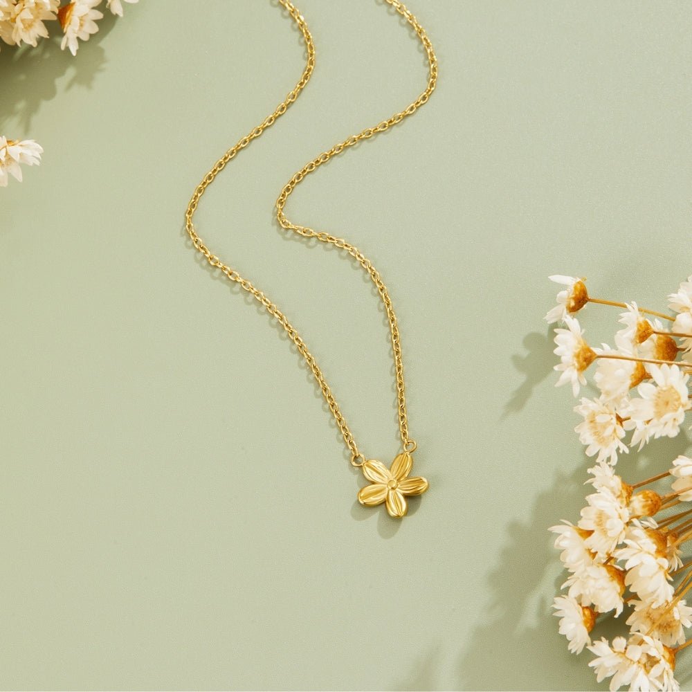 Golden Blossom Pendant Necklace, laid flat on sage green with dried white flowers around it