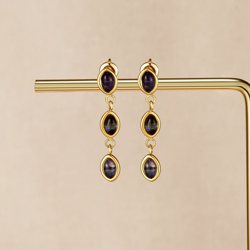 Golden Iridescent Drop Earrings, hanging from a gold display bar, three dark iridescent stones each