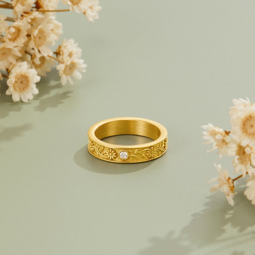 Golden Sculpted Flower Band Ring, standing upright on sage green with dried flowers around it