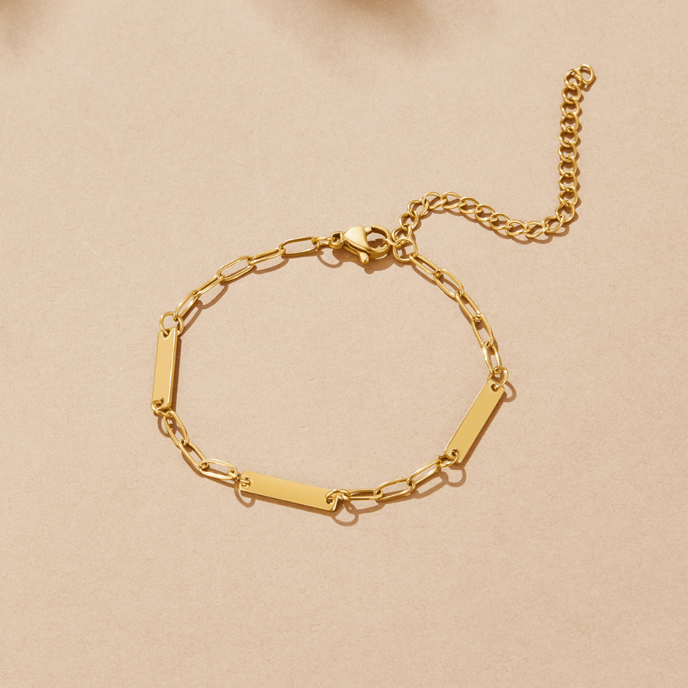Hailey Gold Chain Bracelet, laid flat on a beige surface, with bar links and an extender chain