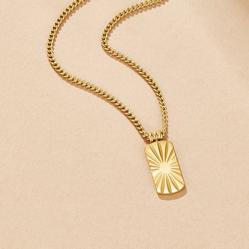 Kiya Gold Pendant Necklace, flat lay on beige, gold curb chain with sunburst tag pendant