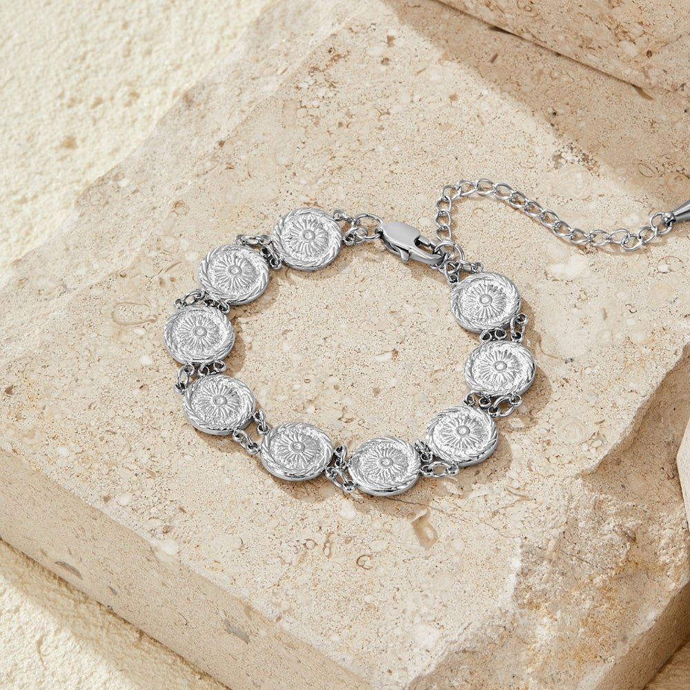 Lara Silver Medallion Bracelet, laid flat on textured stone, round medallions with floral