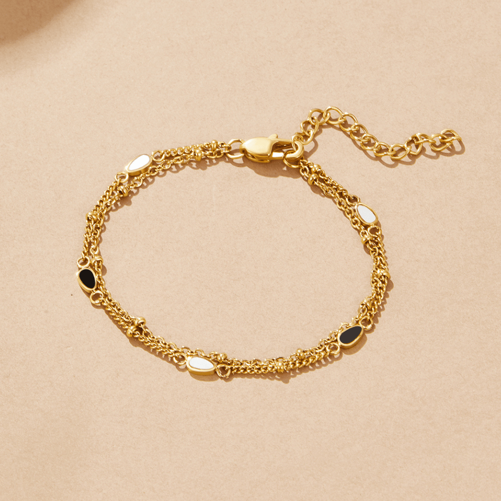 Layered Black & White Stone Bracelet, flat lay of gold double-chain bracelet on beige, with