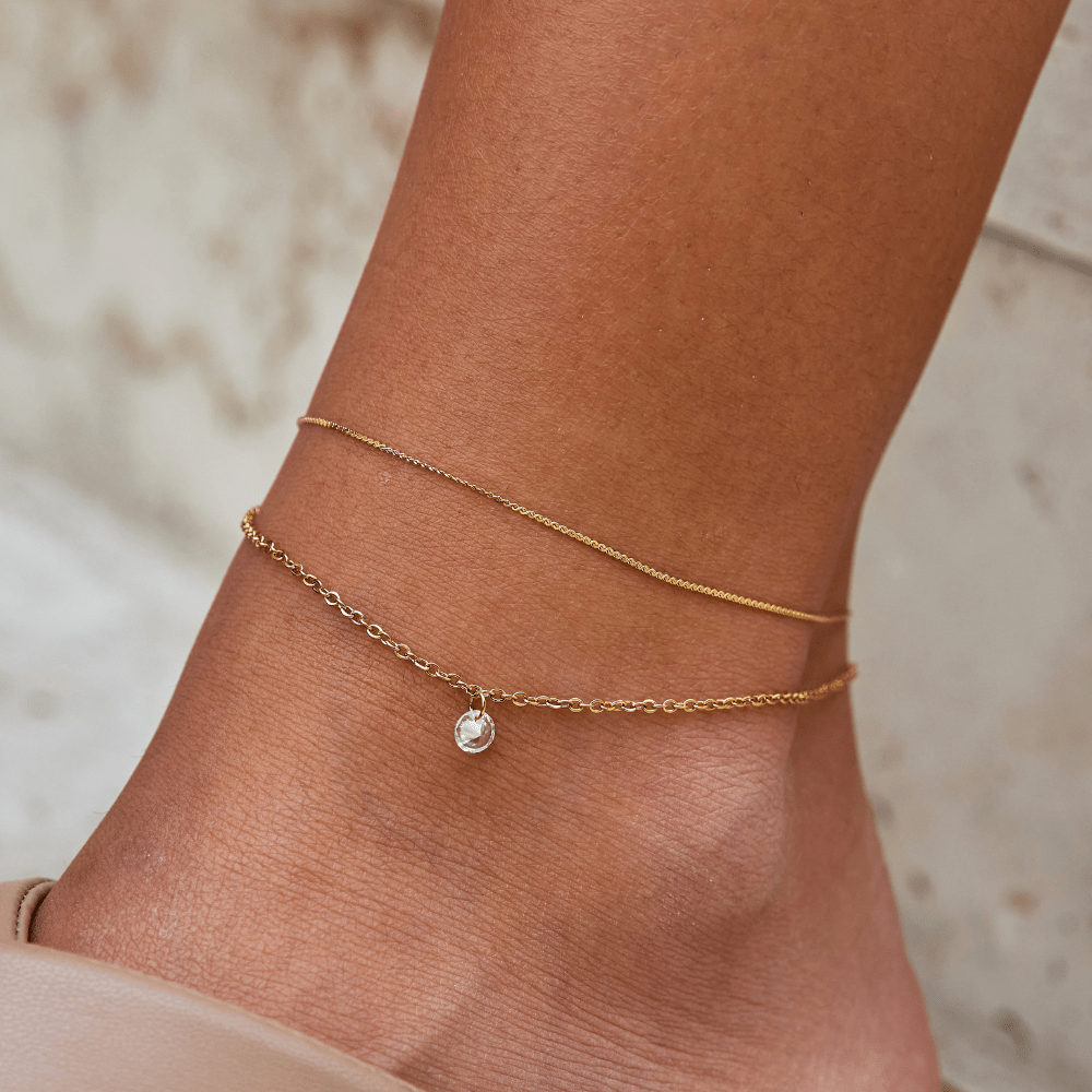 Layered Dainty Crystal Anklet, worn on an ankle with a thin gold chain and a small clear charm
