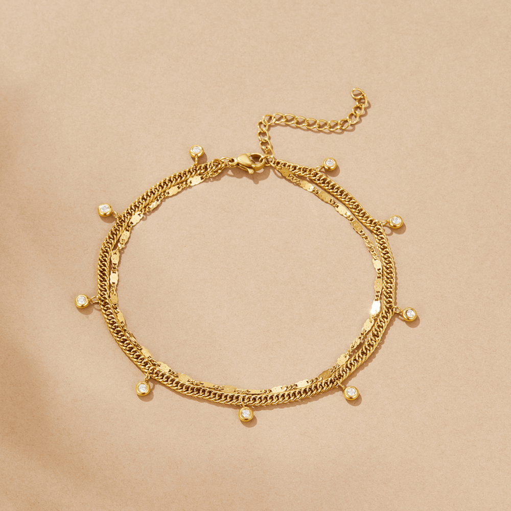 Layered Sabina Gold Anklet, laid flat on beige paper, two gold chains with small crystal drops
