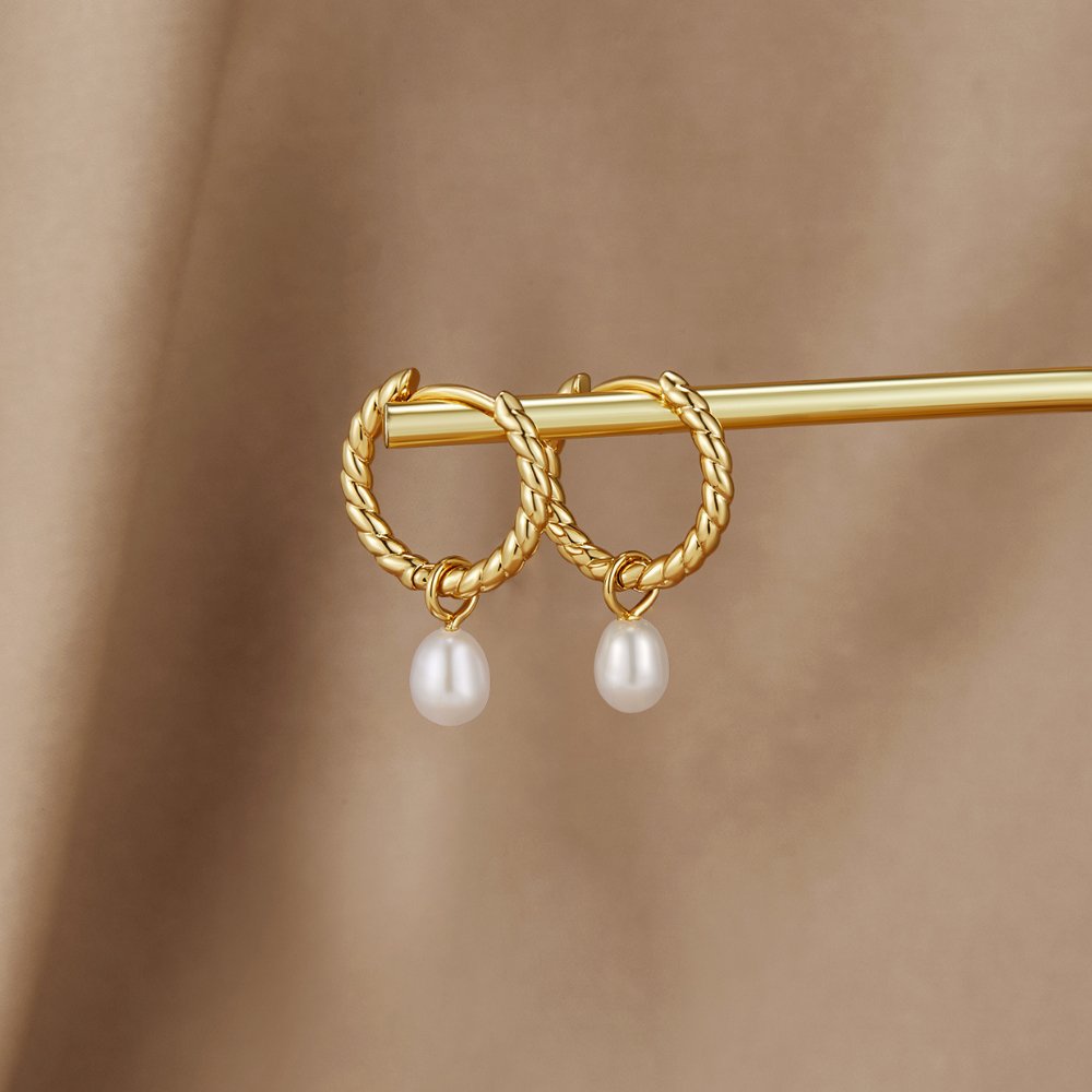 Layla Pearl Twist Earrings, pair of twisted gold hoops with pearl drops, resting on a gold bar