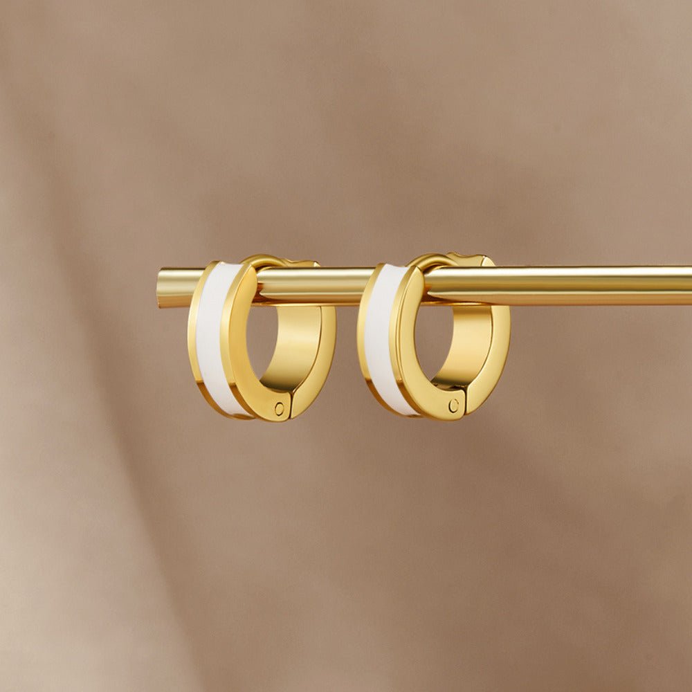 Leigh White Hoop Earrings, hanging on a gold rod against a beige backdrop, white enamel stripe