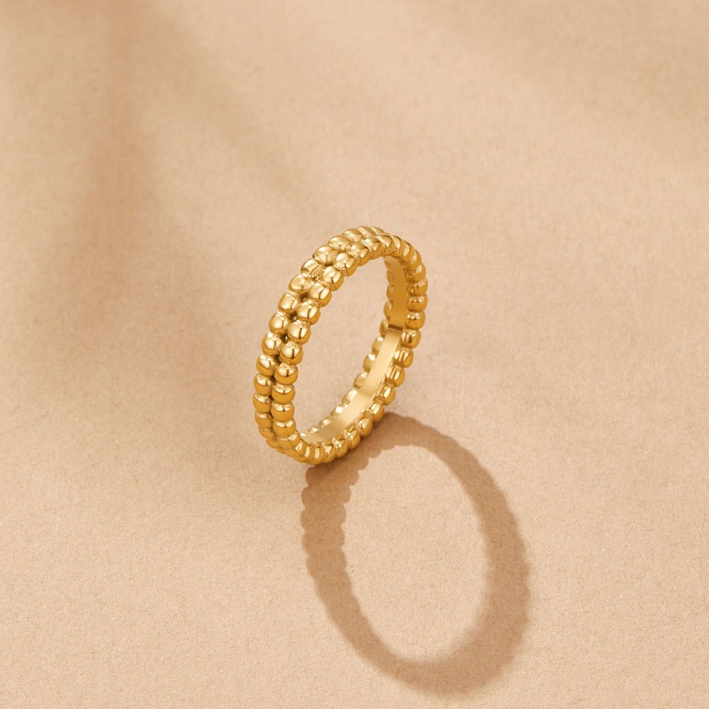 Leona Gold Bead Ring, standing upright on beige surface, casting a shadow, gold beaded band