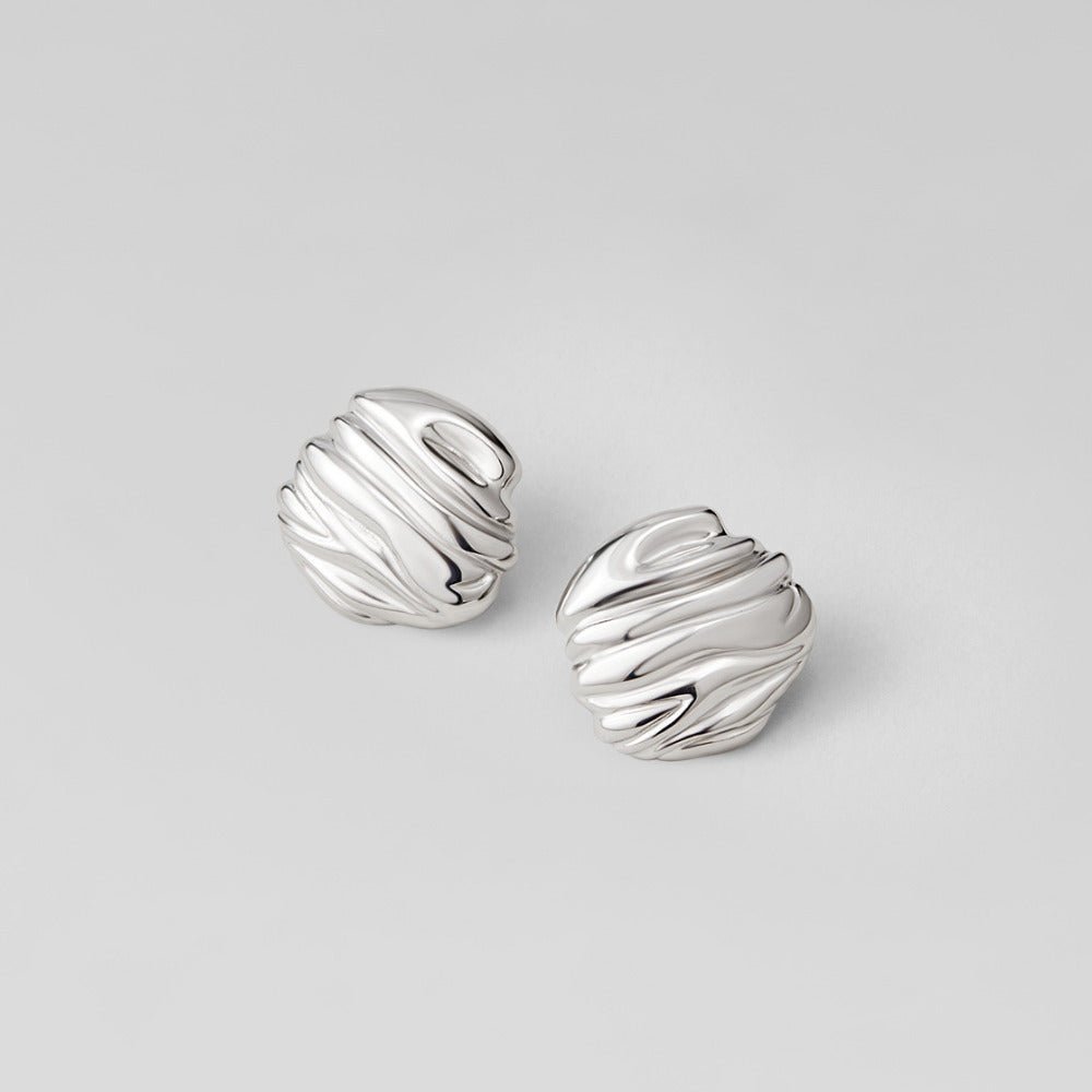 Lila Pleated Silver Button Earrings, a pair of sculpted silver earrings on a pale grey surface